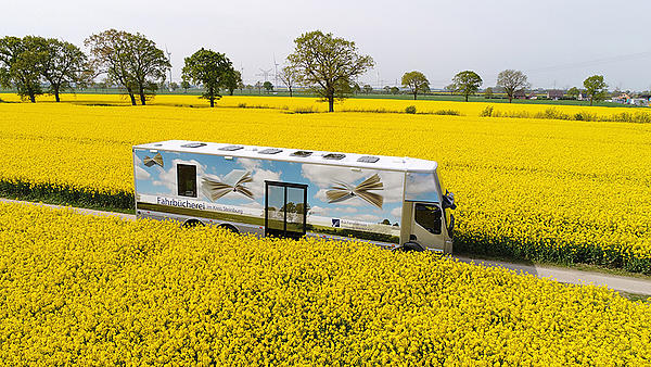 Ein Bücherbus des Büchereizentrale Schleswig-Holstein fährt durch ein Rapsfeld.